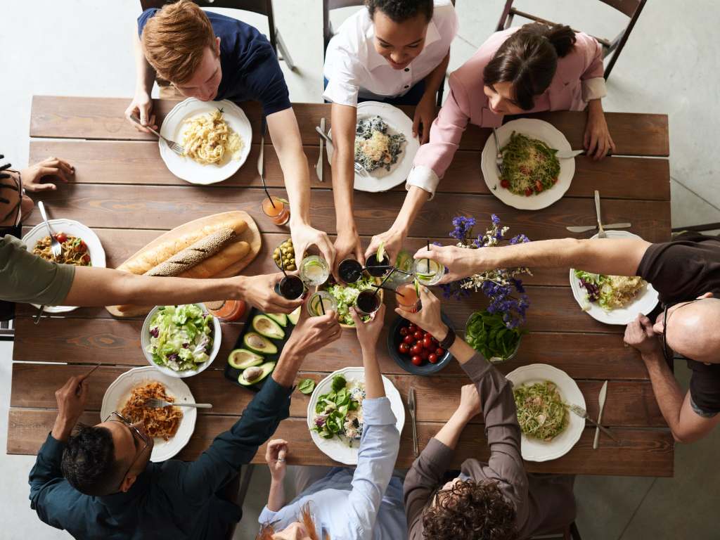 A lively dinner table filled with diverse dishes, friends toasting with drinks, and fresh salads, showcasing a festive atmosphere.